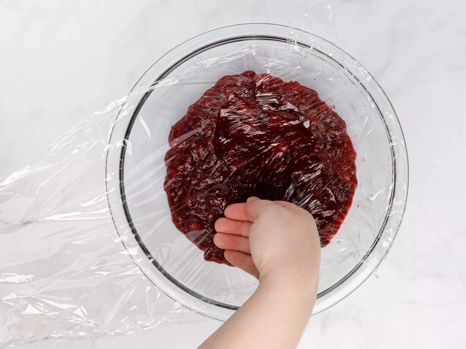 Clear bowl of cranberry chutney getting covered with plastic wrap