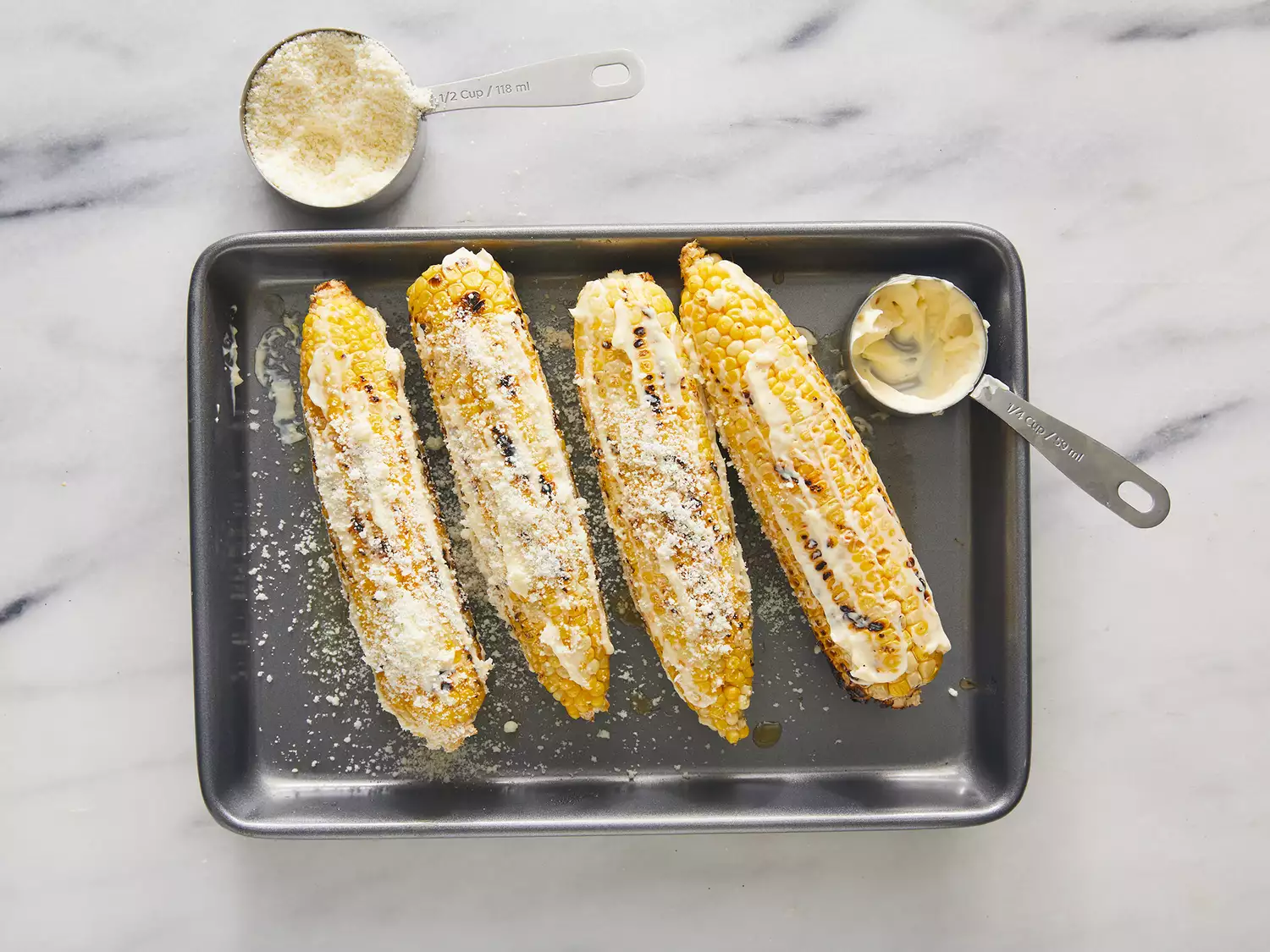 Overhead of Elote being covered in cotija cheese on a baking sheet.
