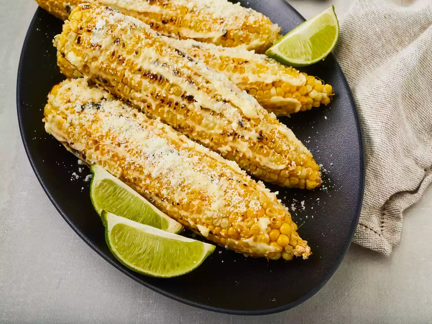 looking down at four Mexican corn on the cobs on a plate with a few lime wedges as garnish
