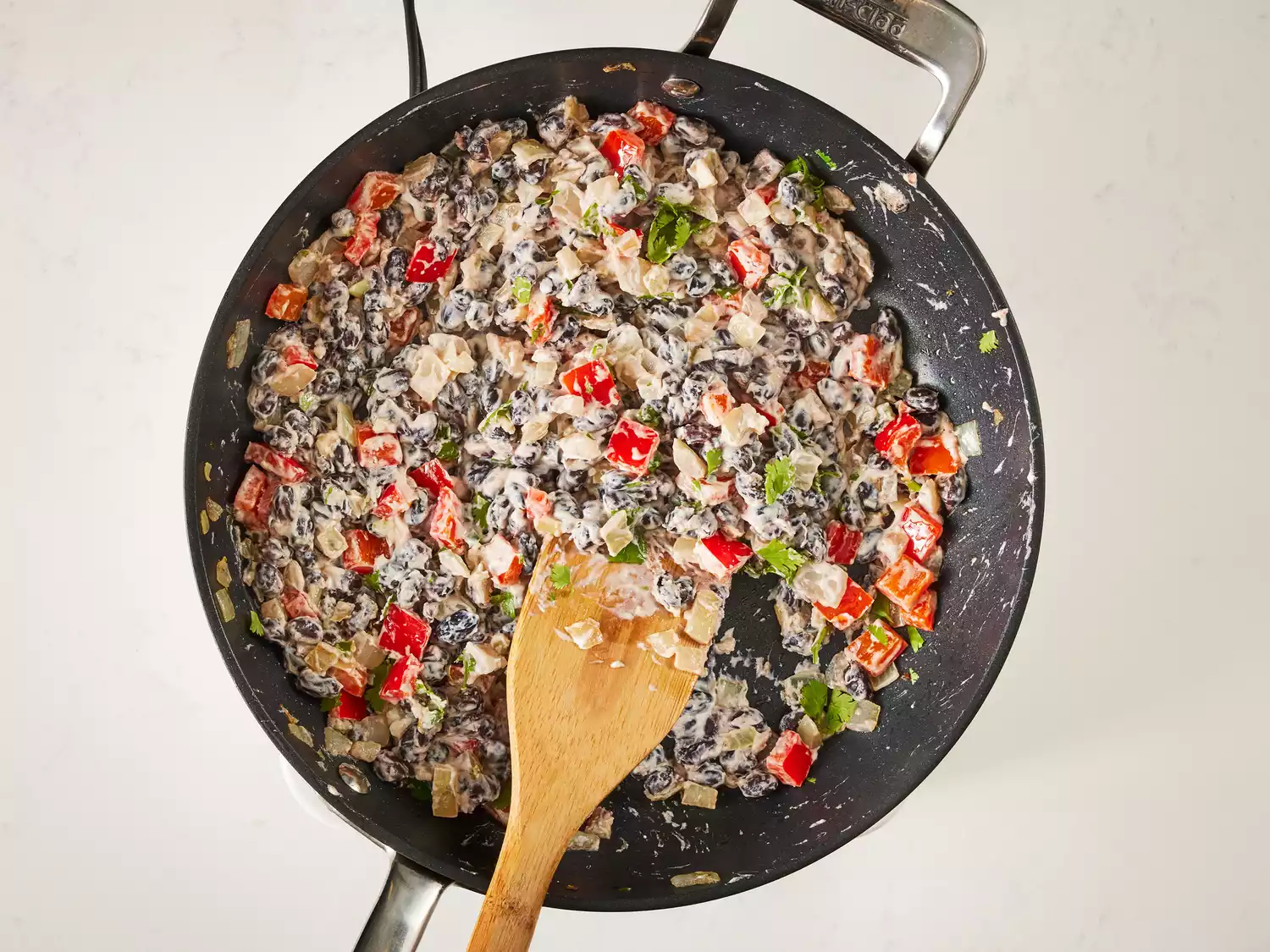 an overhead shot of black beans and cream cheese added to veggies in a pan