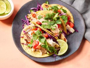 Grilled fish tacos with chipotle lime dressing garnished with cilantro and a lime wedge on a plate