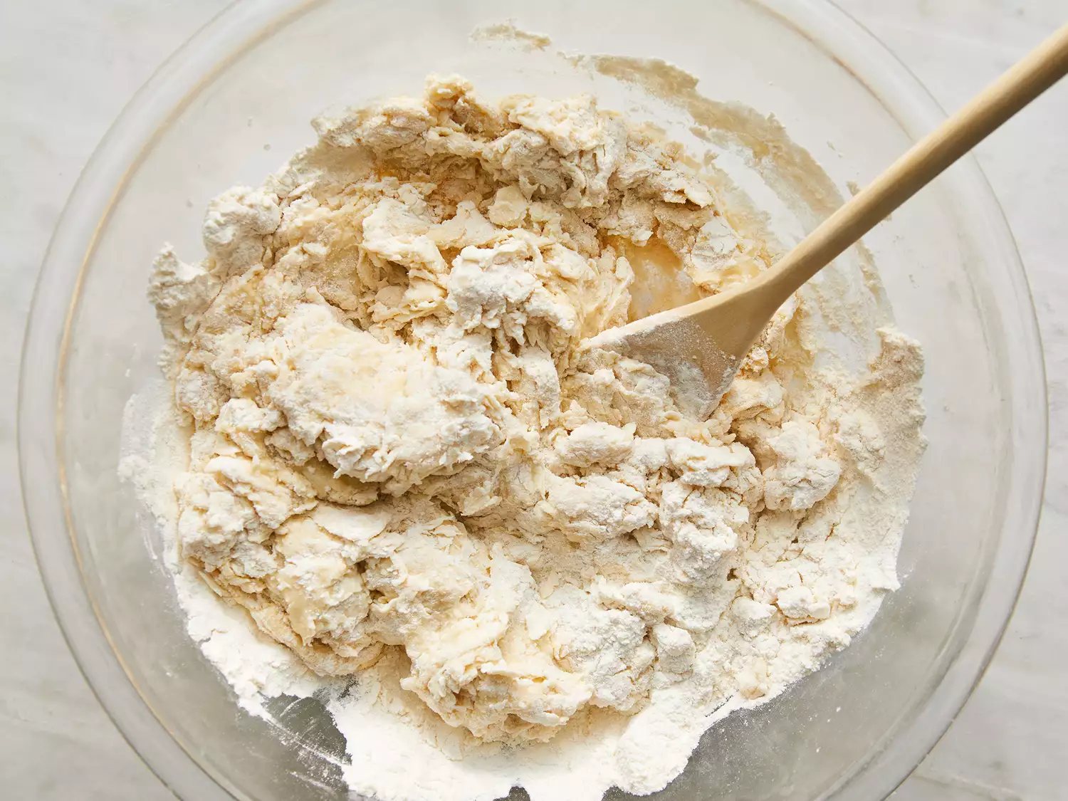 Overhead shot of a mixing bowl with naan dough being stirred with a wooden spoon