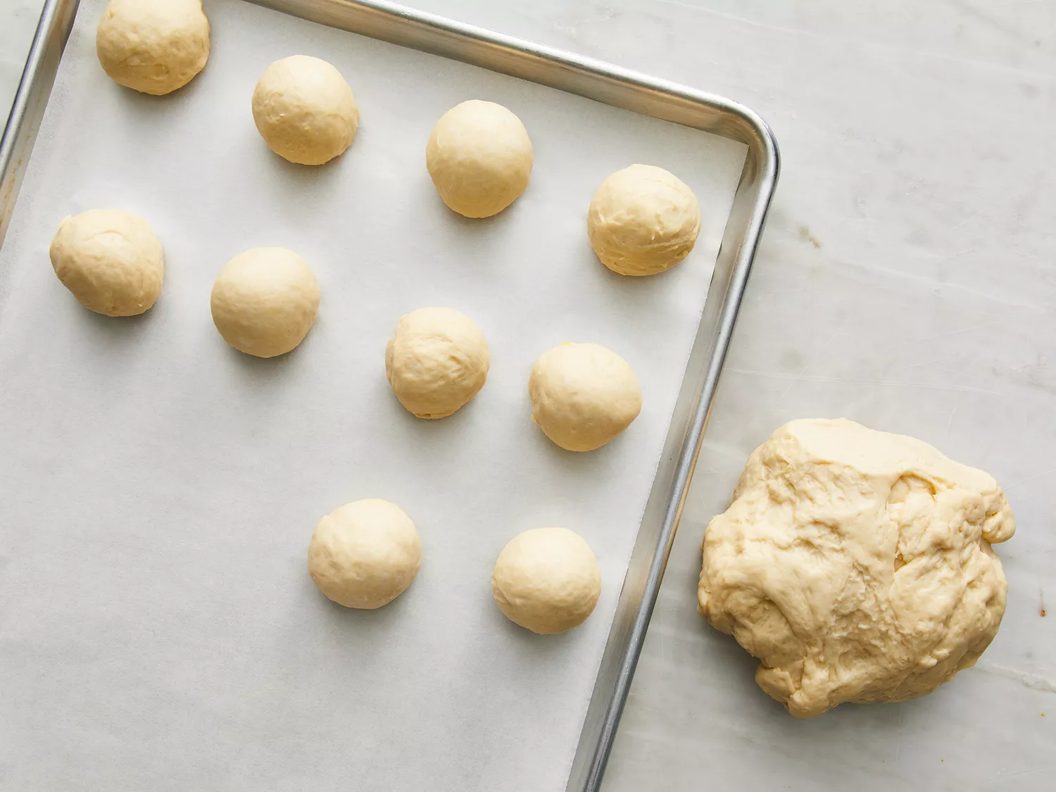 Overhead shot of naan dough being rolled into balls on a baking sheet