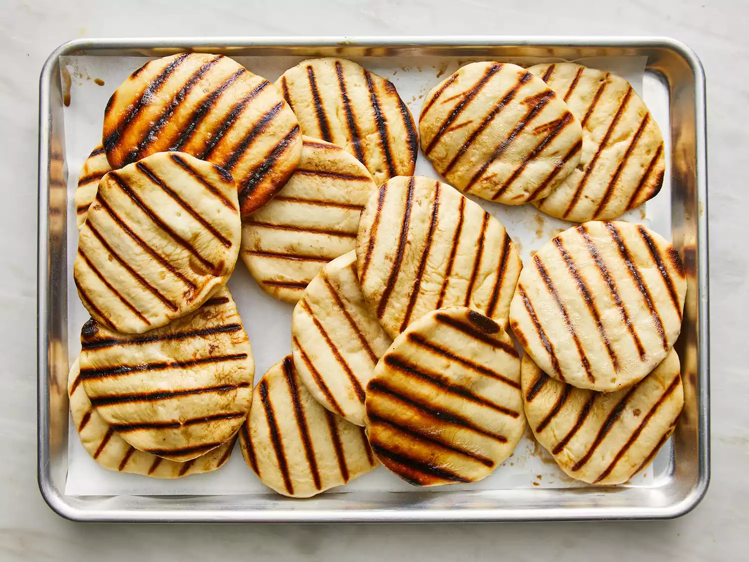 Overhead shot of grilled naan bread on a baking sheet