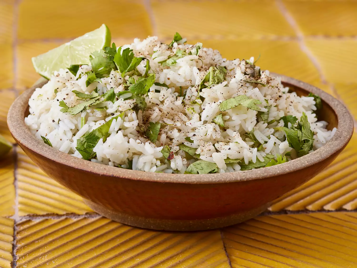 Mid low angle looking at a heaping bowl of lime cilantro rice garnished with a lime wedge