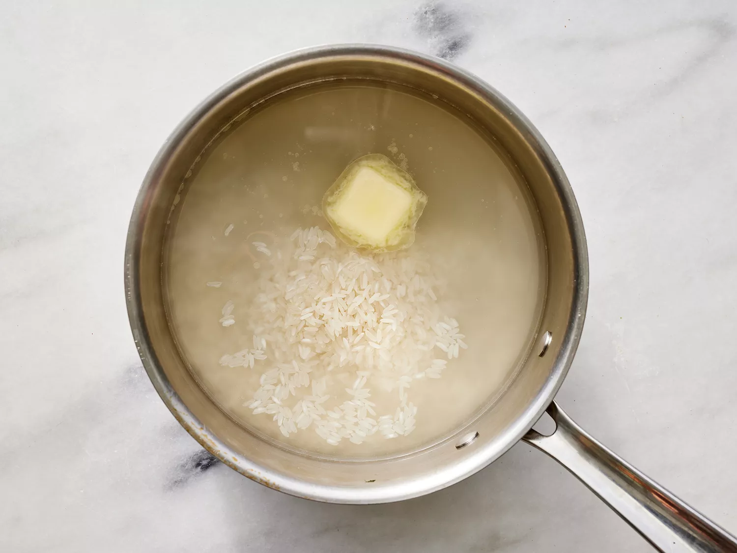 Butter and rice stirred into boiled water in a saucepan. 