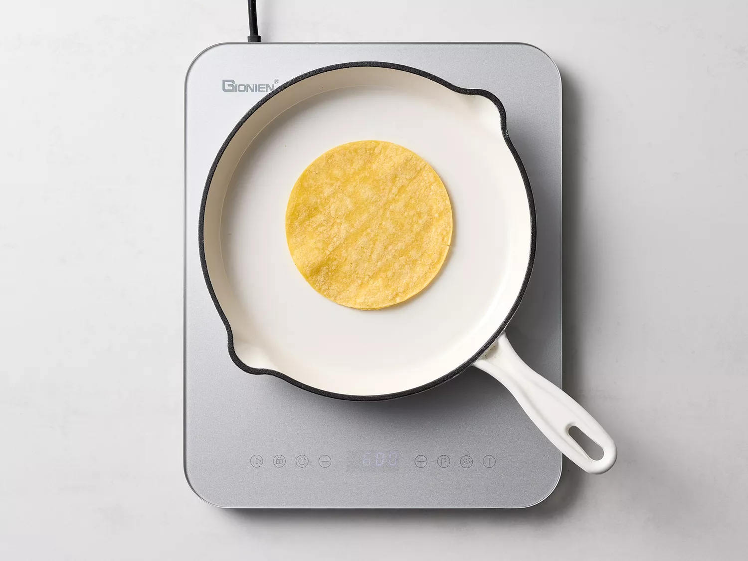 A corn tortilla heating in a white skillet on a stovetop