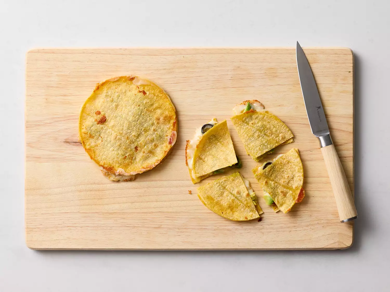 A quesadilla being cut into triangular pieces on a wooden board