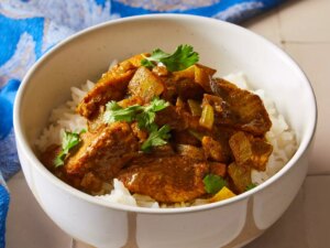 Easy chicken curry over white rice, garnished with fresh herbs in a white bowl