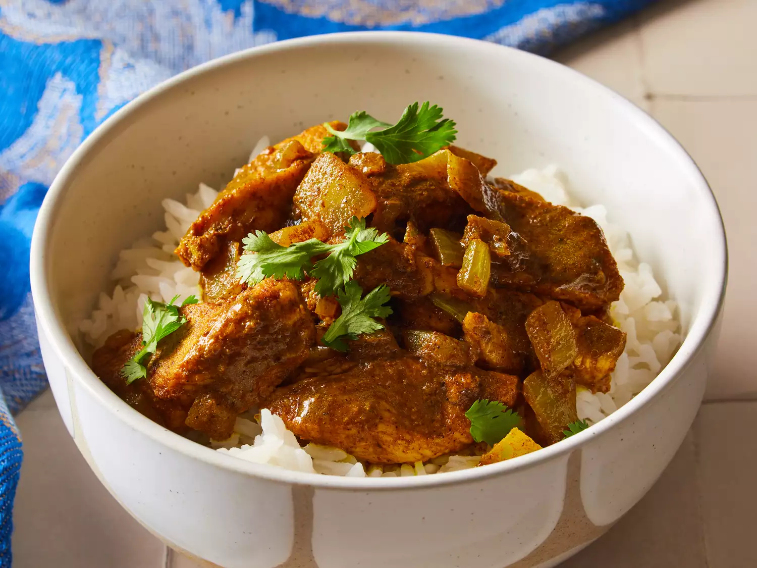 Easy chicken curry over white rice, garnished with fresh herbs in a white bowl
