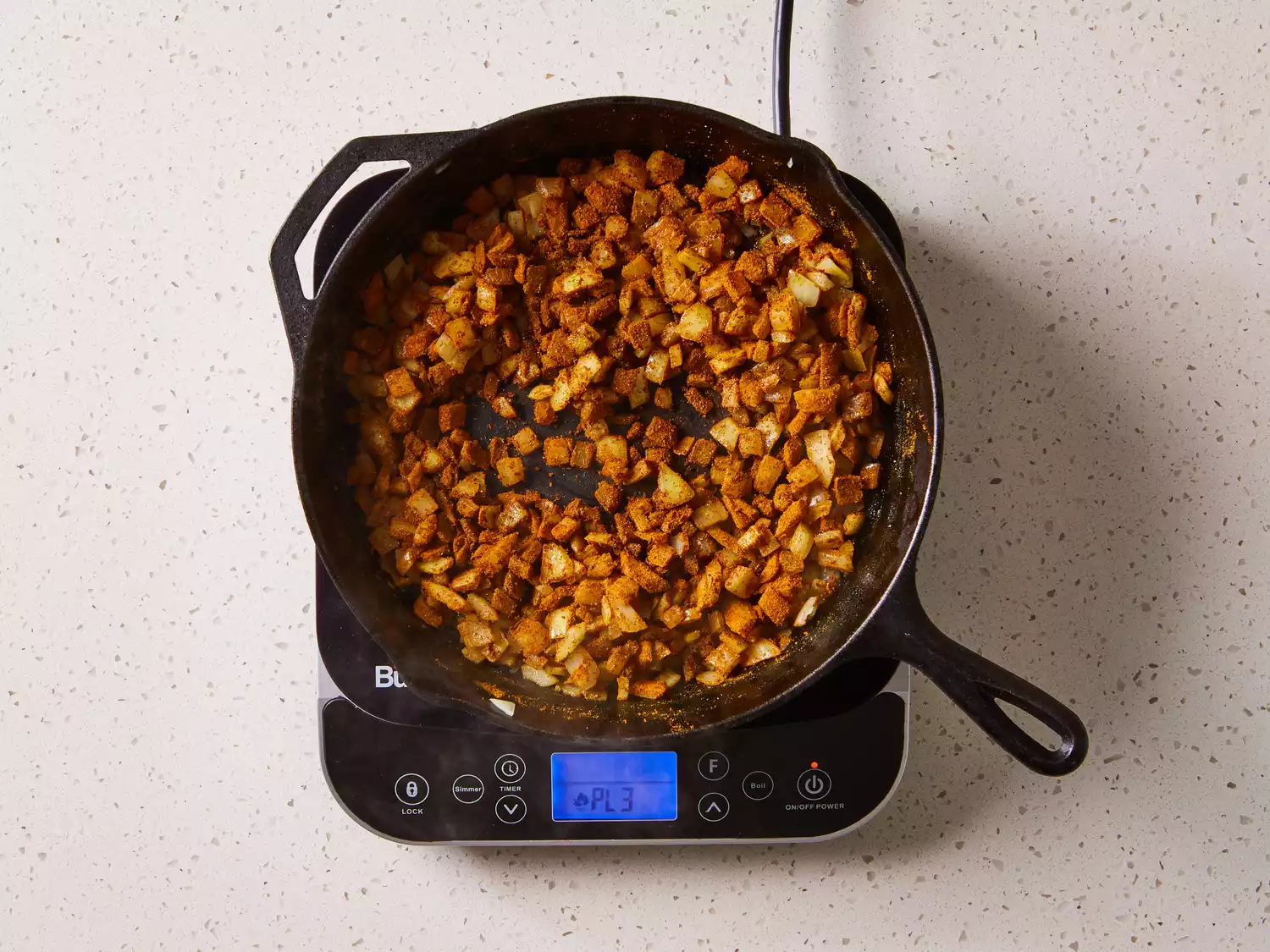 Onions with curry powder cooking in a cast iron skillet on a burner 