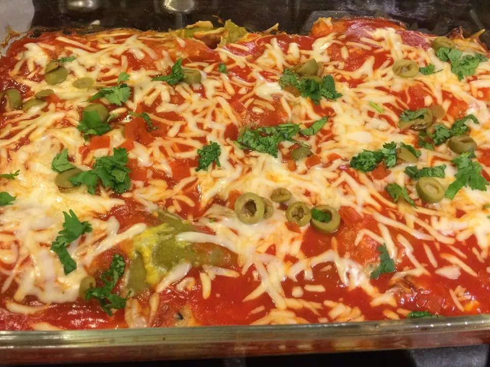 Close up view of chili relleno casserole garnished with sliced green olives and fresh herbs in a glass baking dish