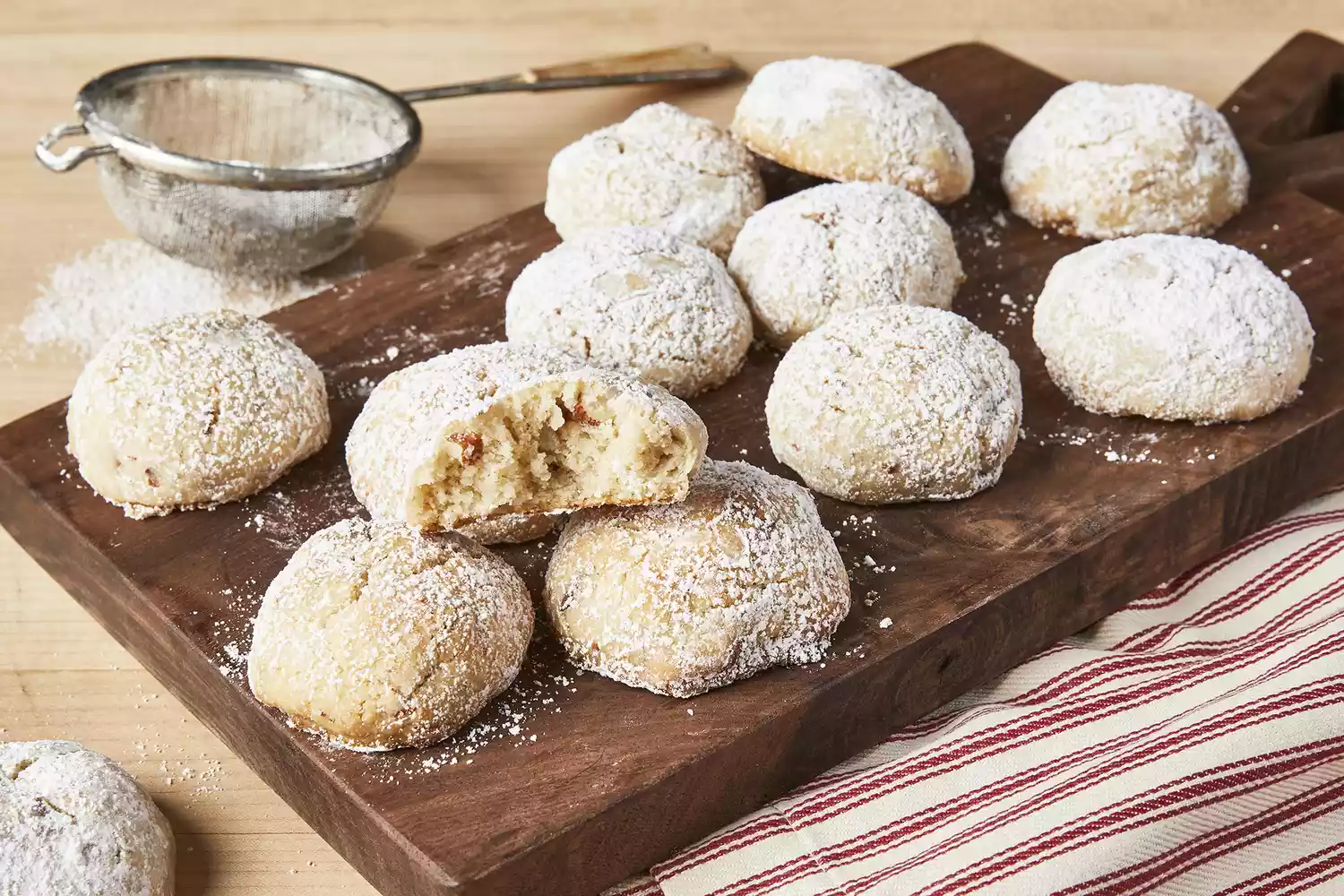 a close up view of a pile of Mexican wedding cookies one with a bite out sits on top.