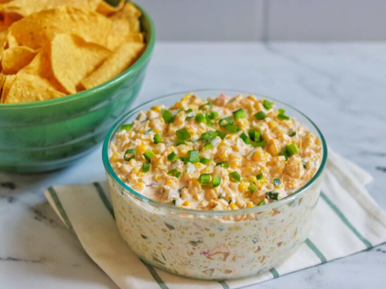 Creamy corn dip in glass bowl with chips on the side and topped with green onions