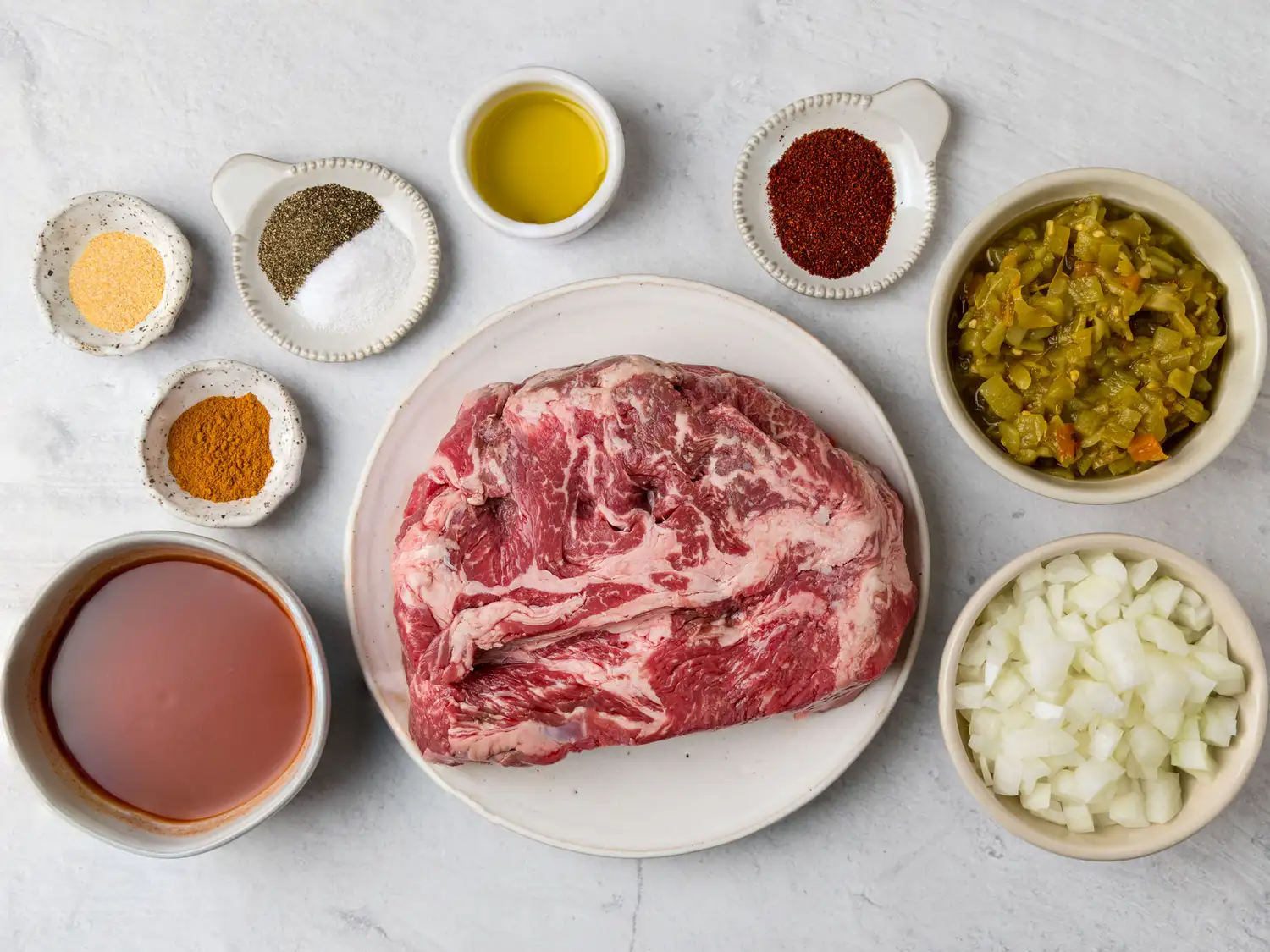 Ingredients for slow cooker Mexicanstyle meat arranged including raw beef seasonings chilies onion and liquid components