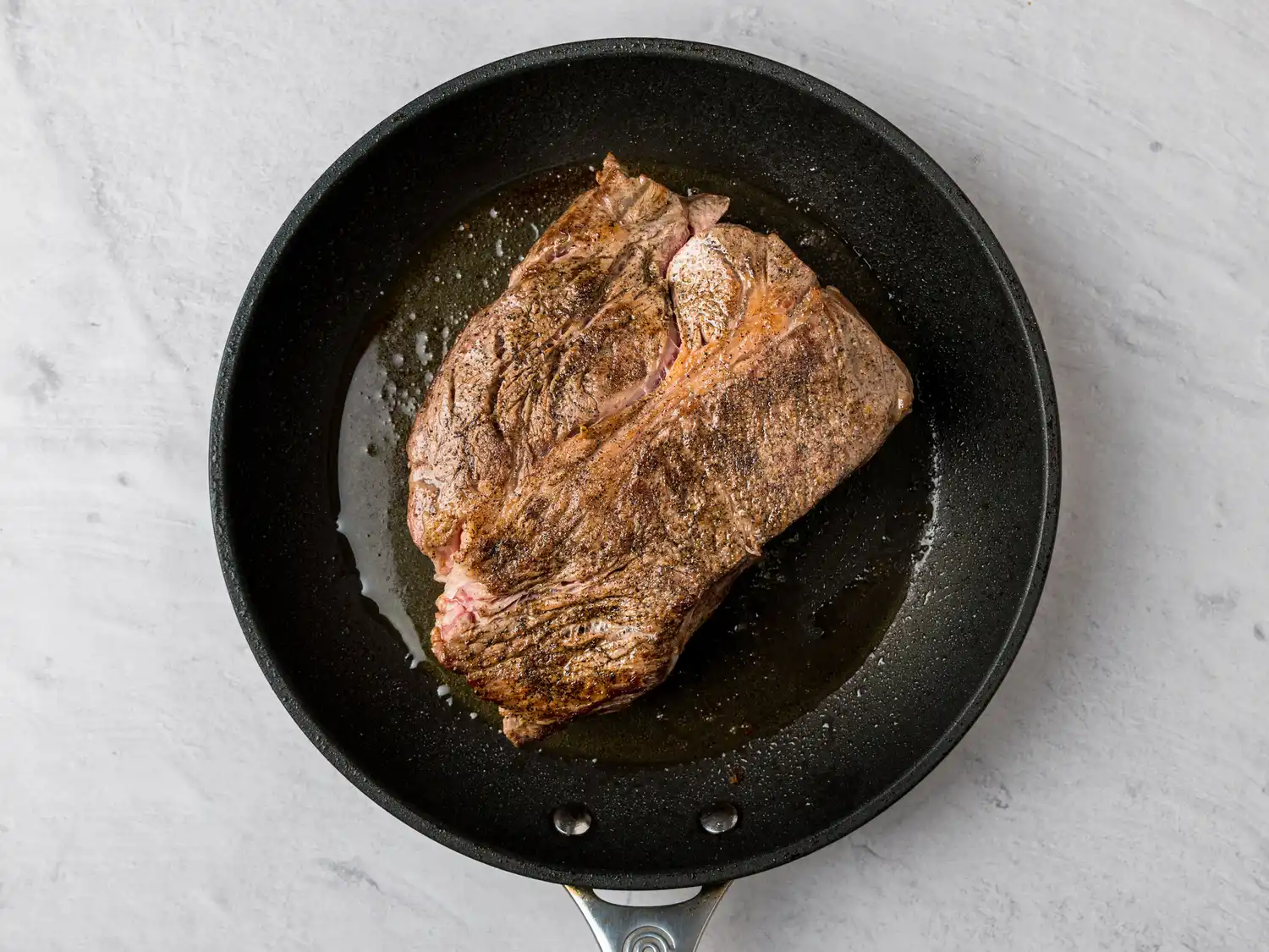 Cooked meat in a black frying pan on a light surface