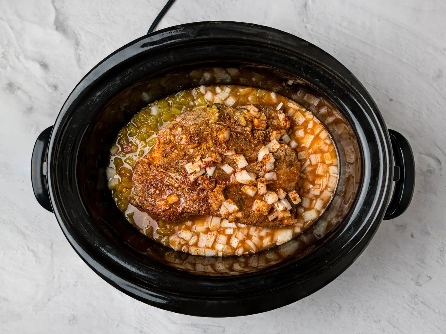 Slow cooker with seasoned meat onions and sauces for a Mexicanstyle dish