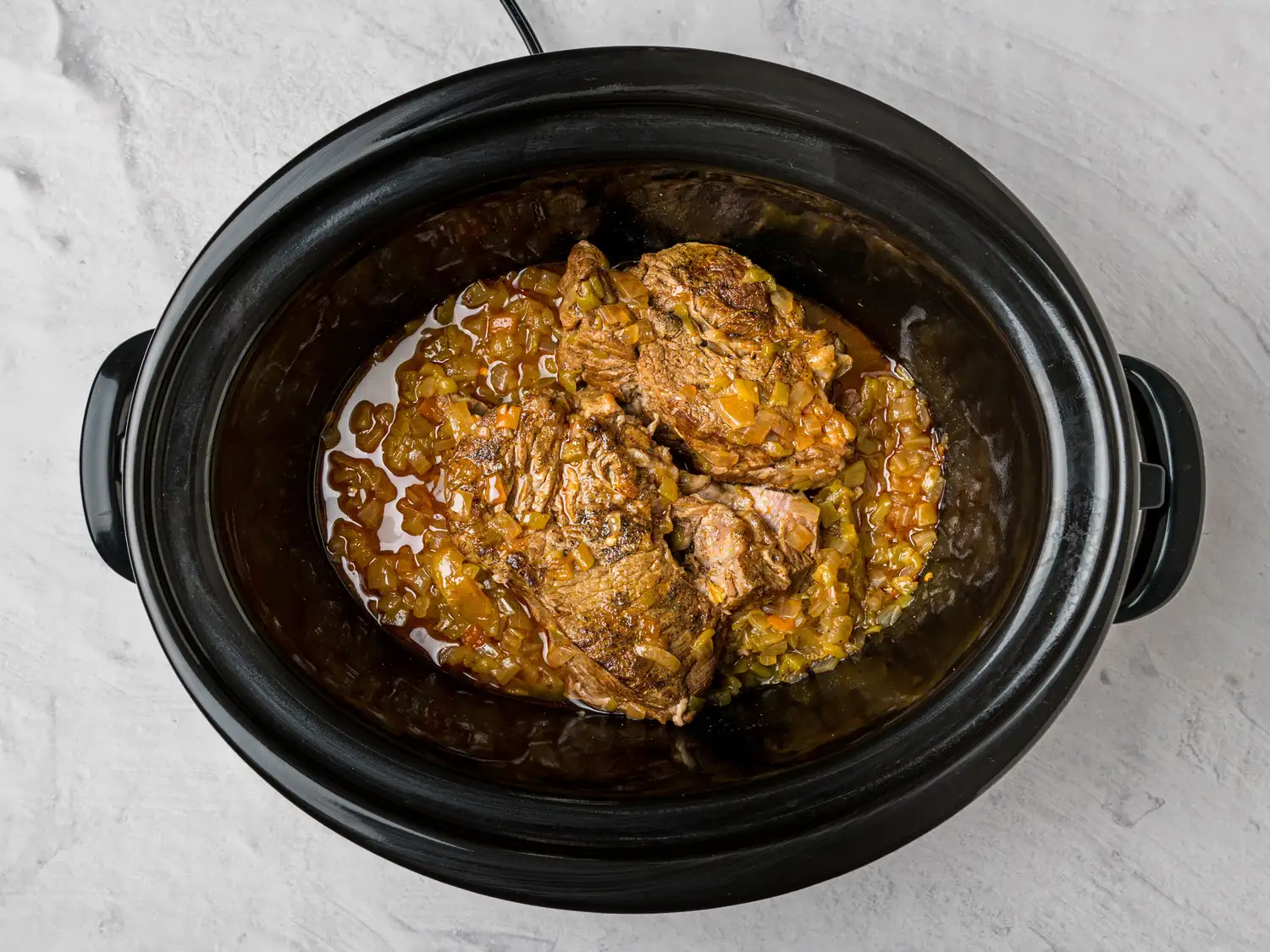 Slow cooker containing seasoned meat and sauce