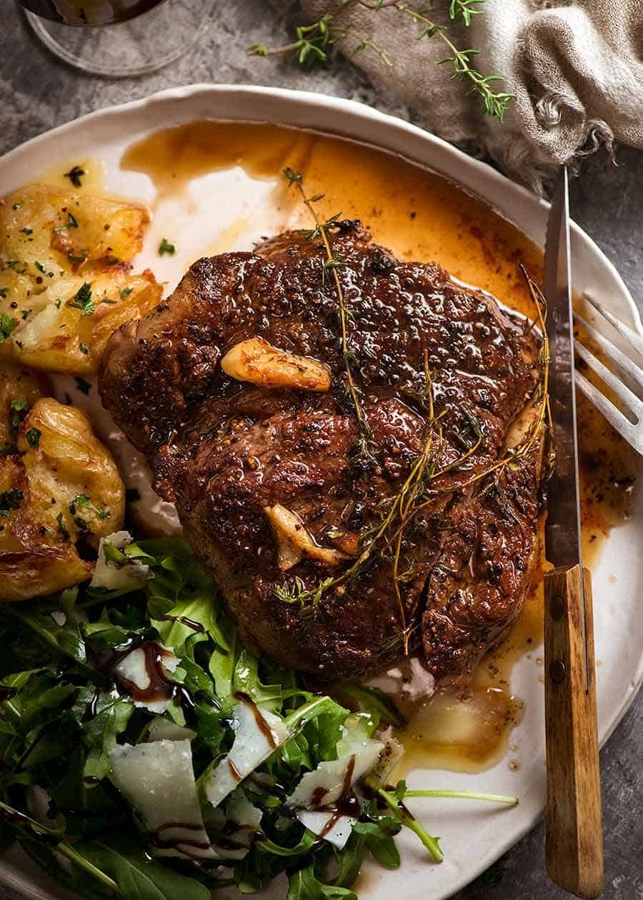 How to Cook Steak – like a chef! Recipe Pan Seared Steak with garlic butter sauce on a plate with a side of crispy smashed potatoes and rocket salad