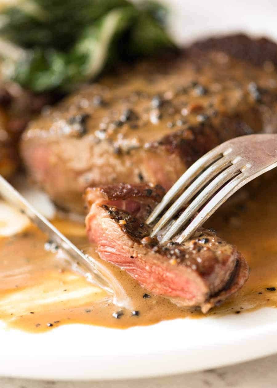Steak with Creamy Peppercorn Sauce Recipe Close up of fork and knife eating a piece of Steak with Creamy Peppercorn Sauce