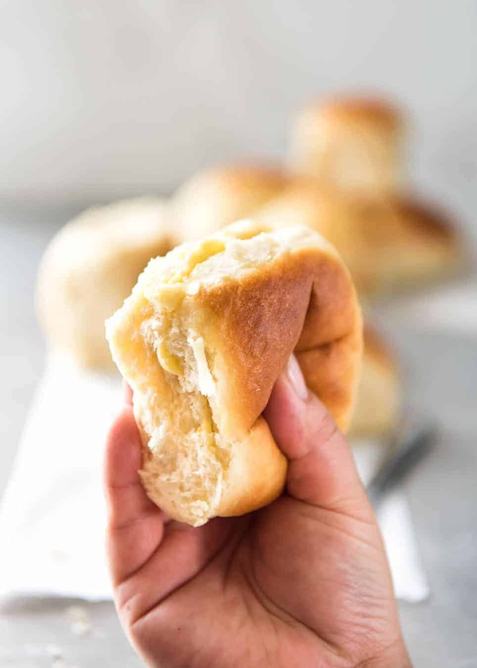 Soft No Knead Dinner Rolls Recipe Hand squeezing no knead dinner rolls to show how soft and fluffy they are.