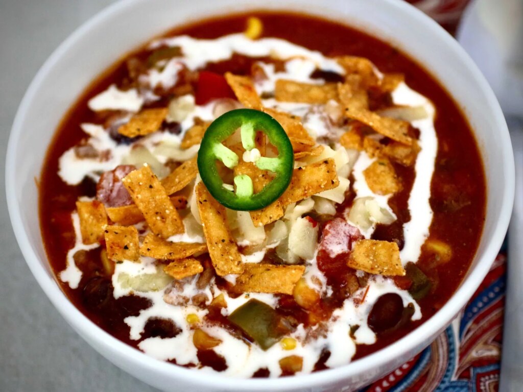 Taco soup topped with tortillas, sour cream and garnished with jalapeno slice