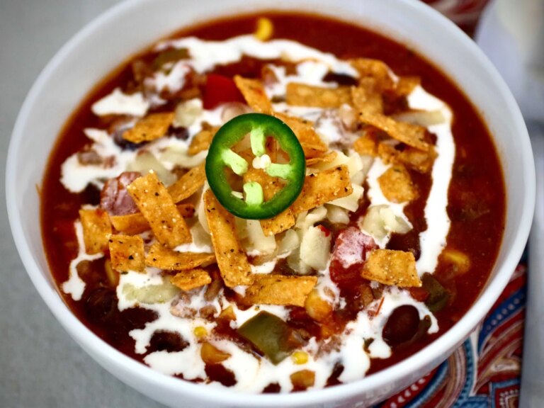 Taco soup topped with tortillas, sour cream and garnished with jalapeno slice