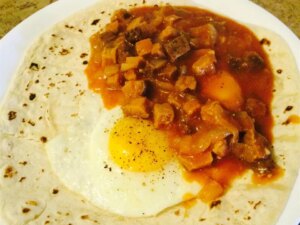 Close up view of a tortilla with a fried egg and pork green chile on a white plate