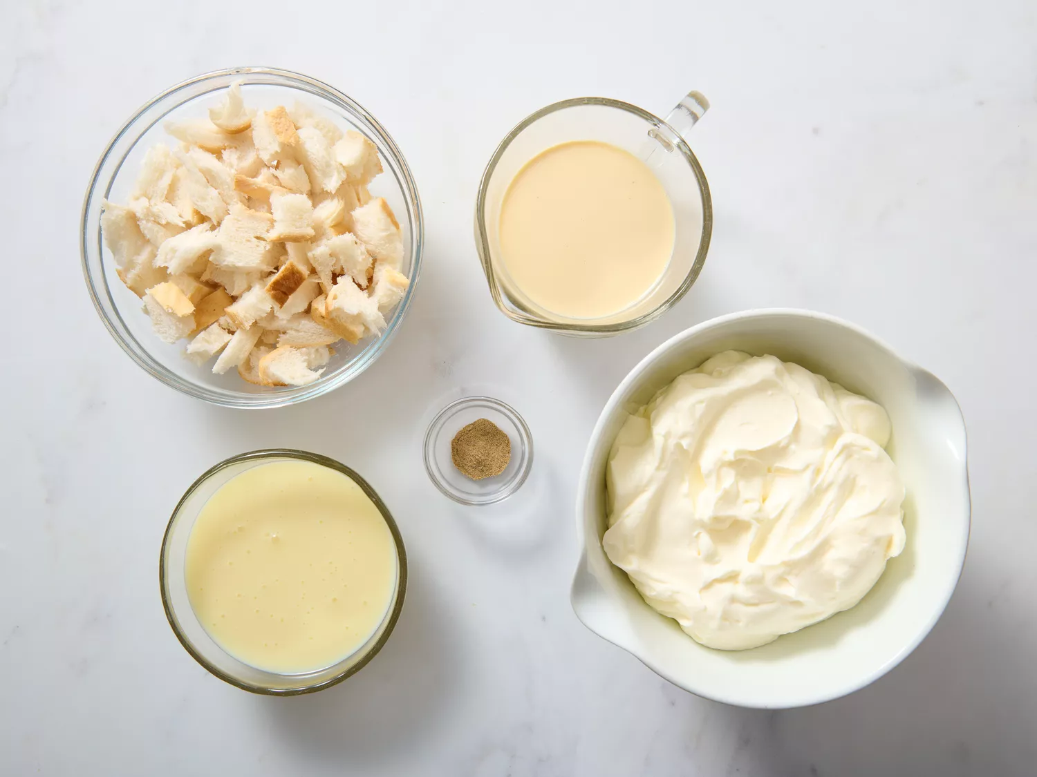 Bowls and containers of ingredients for a recipe including cream, condensed milk, and chopped bread