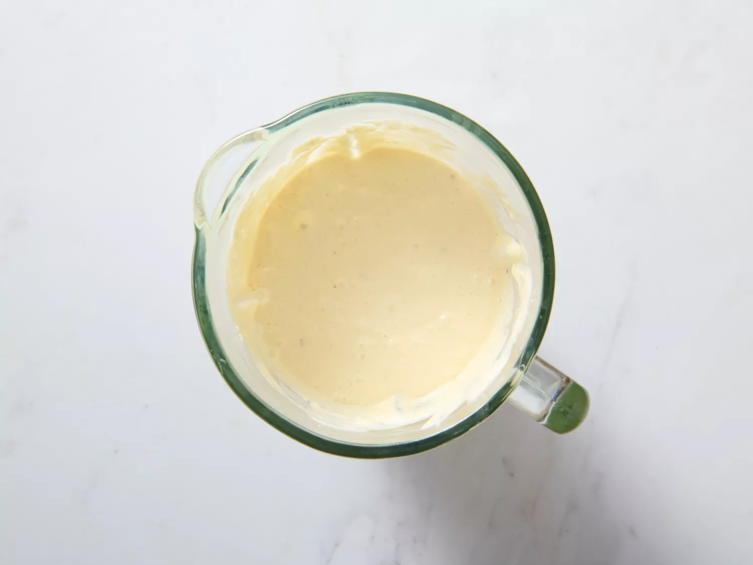 A blender with creamy yellow mixture inside, placed on a white surface