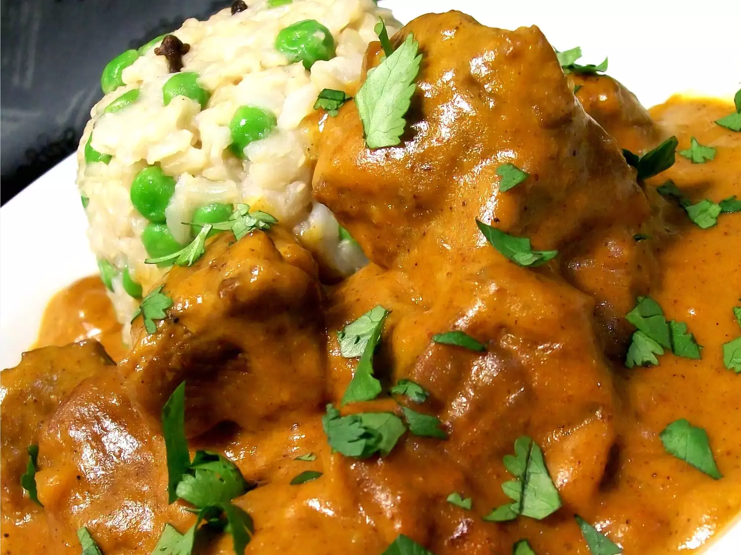 Close up view of butter lamb gravy garnished with fresh herbs, served with rice and peas on a plate
