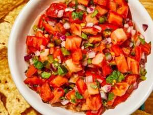 A super close up overhead view of fresh pico de gallo in a white bowl, with chips on the side