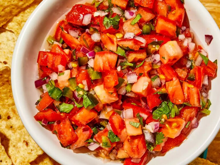 A super close up overhead view of fresh pico de gallo in a white bowl, with chips on the side