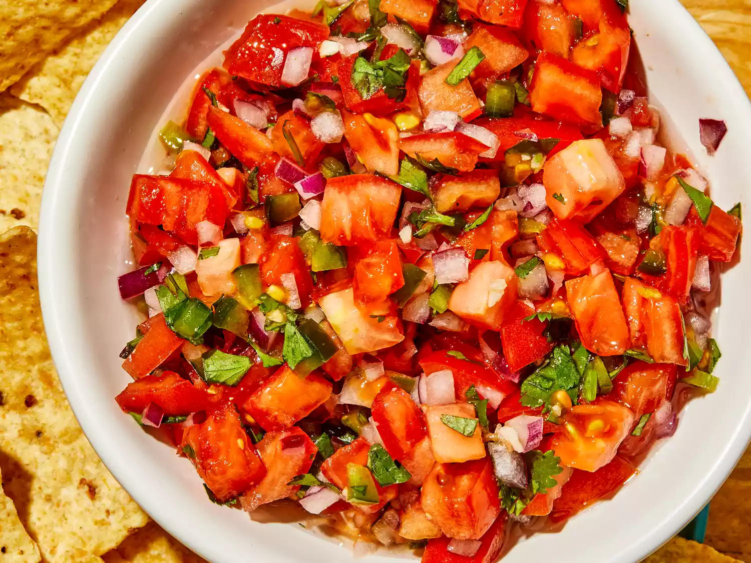A super close up overhead view of fresh pico de gallo in a white bowl, with chips on the side