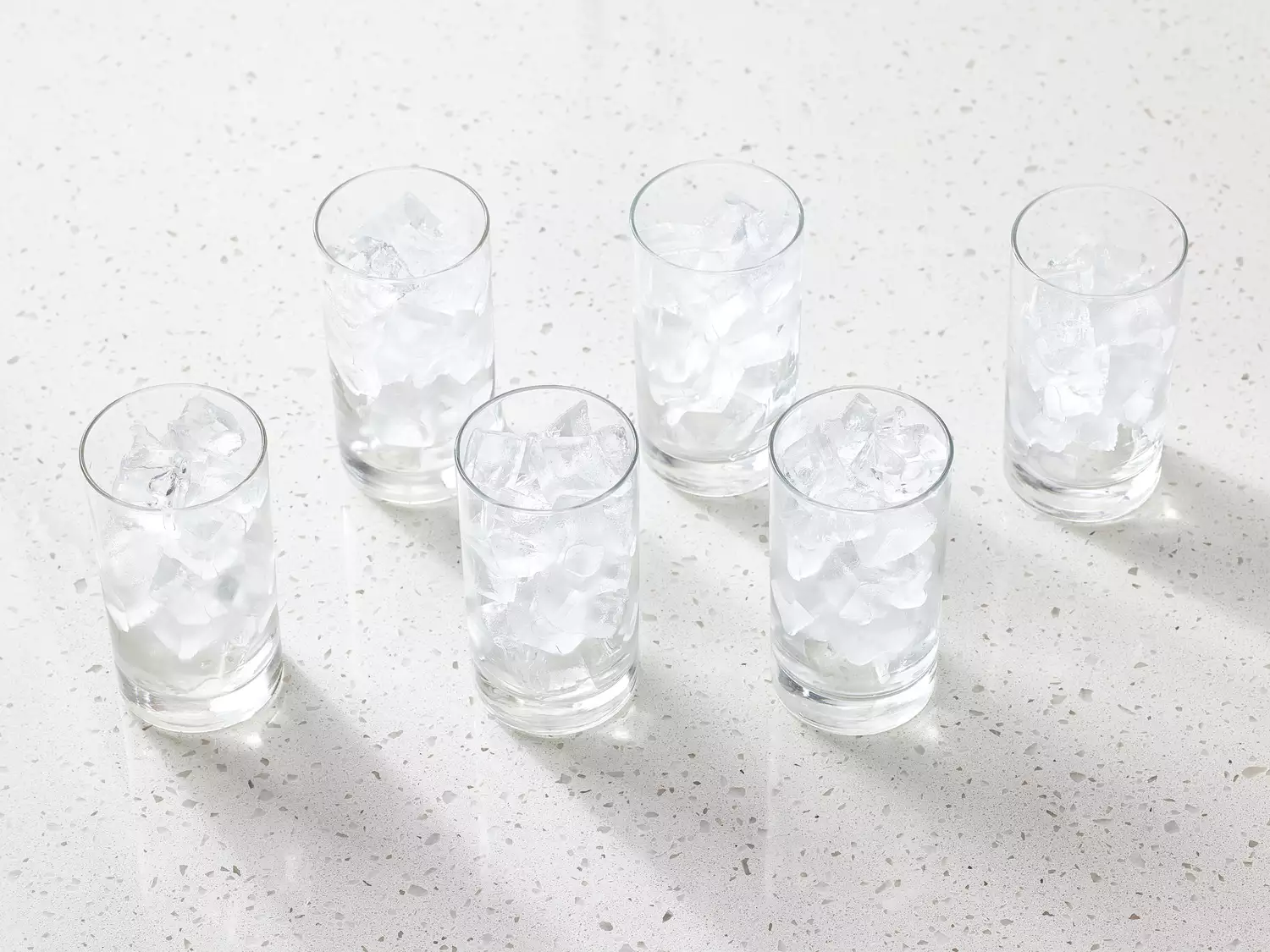 Six glasses filled with ice cubes arranged on a countertop