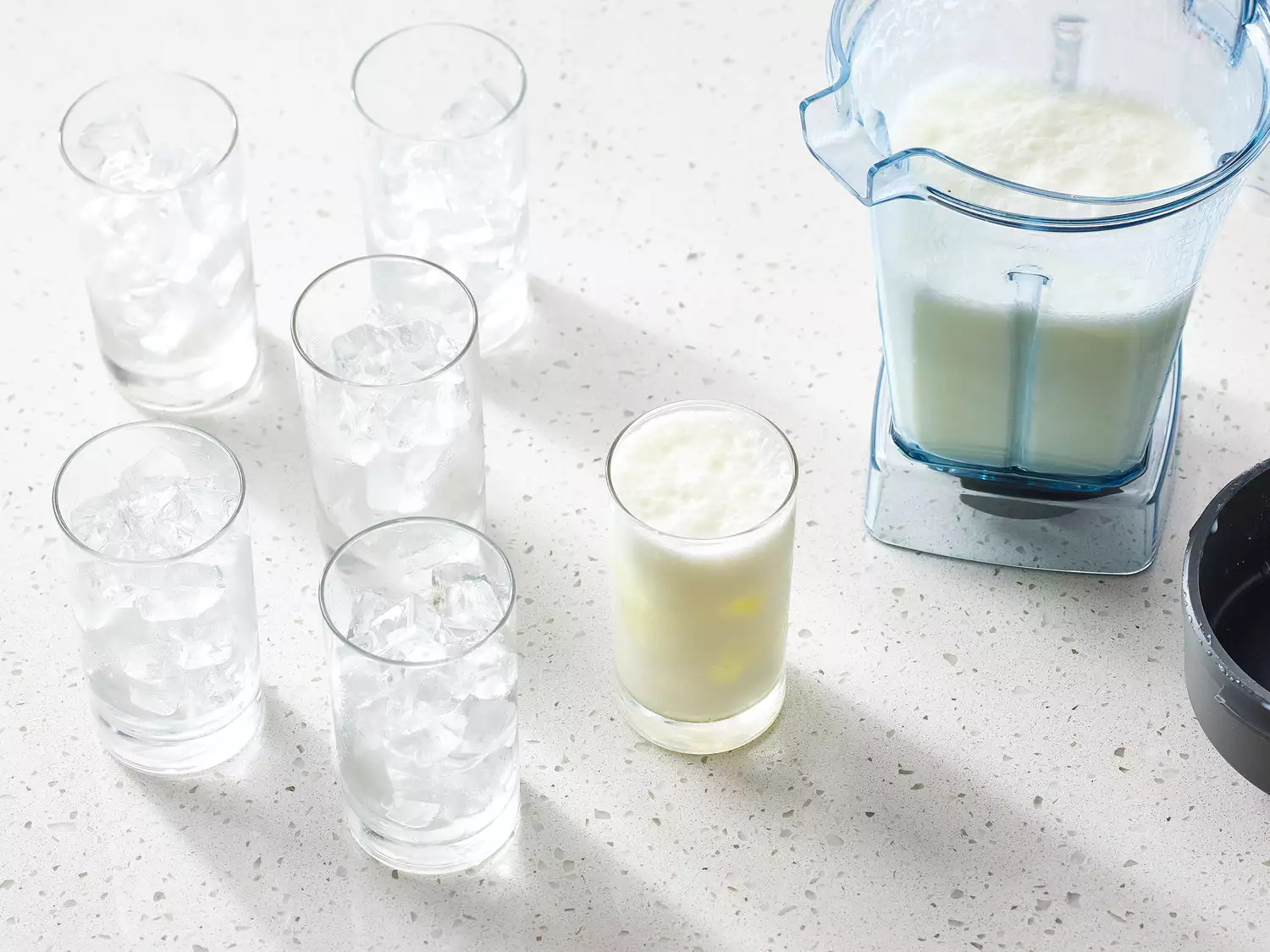 A blender with an Indian lassi and six glasses, one filled