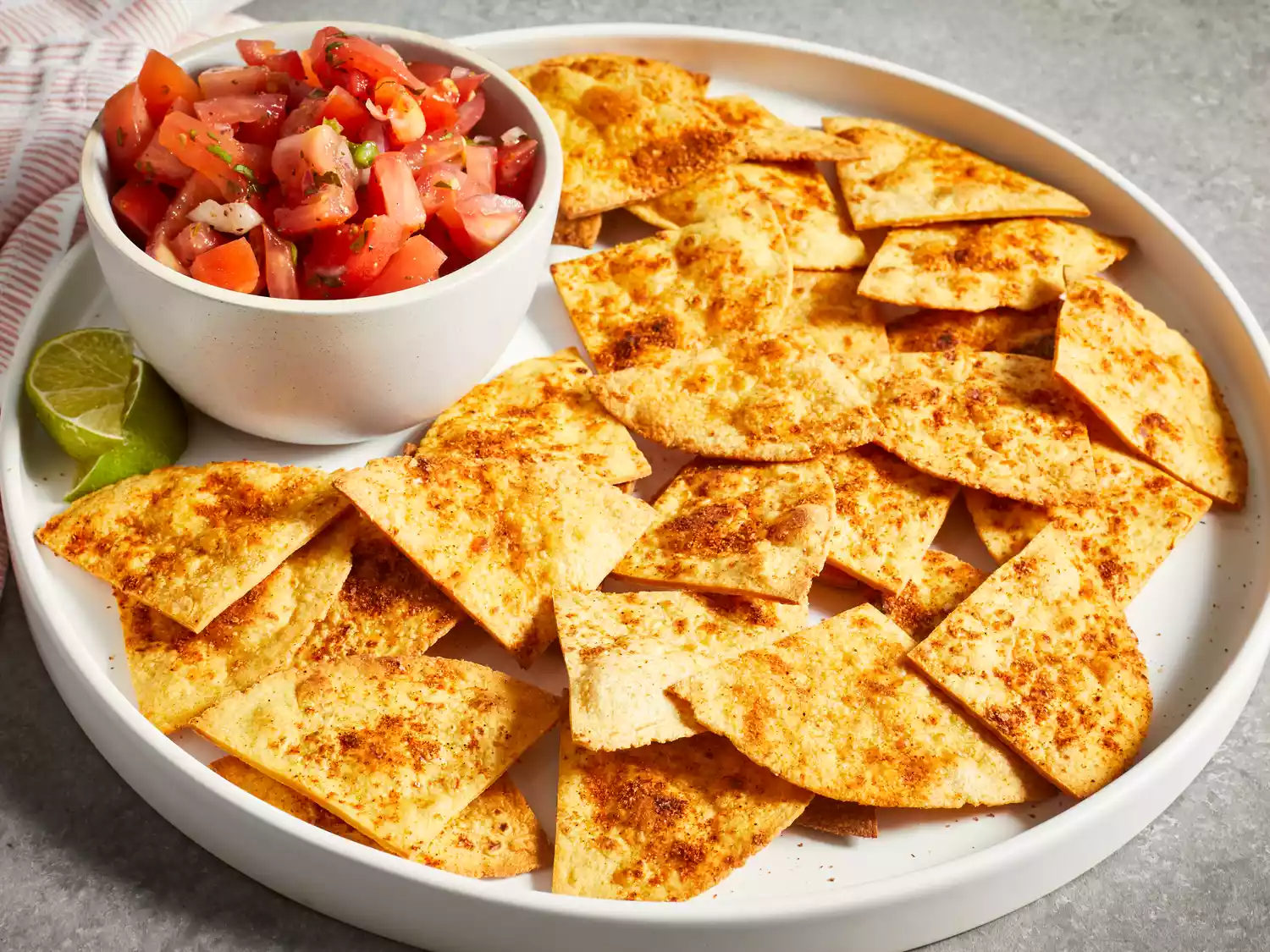 A low angle view of a platter of golden brown baked tortilla chips served with a side of fresh salsa.