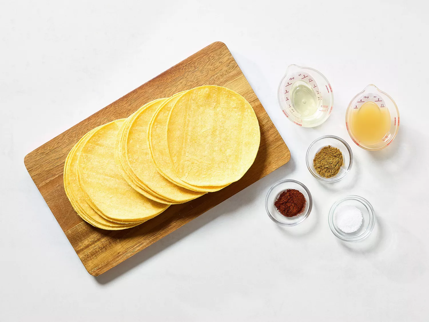 Corn tortillas with seasonings and liquids on a wooden board.