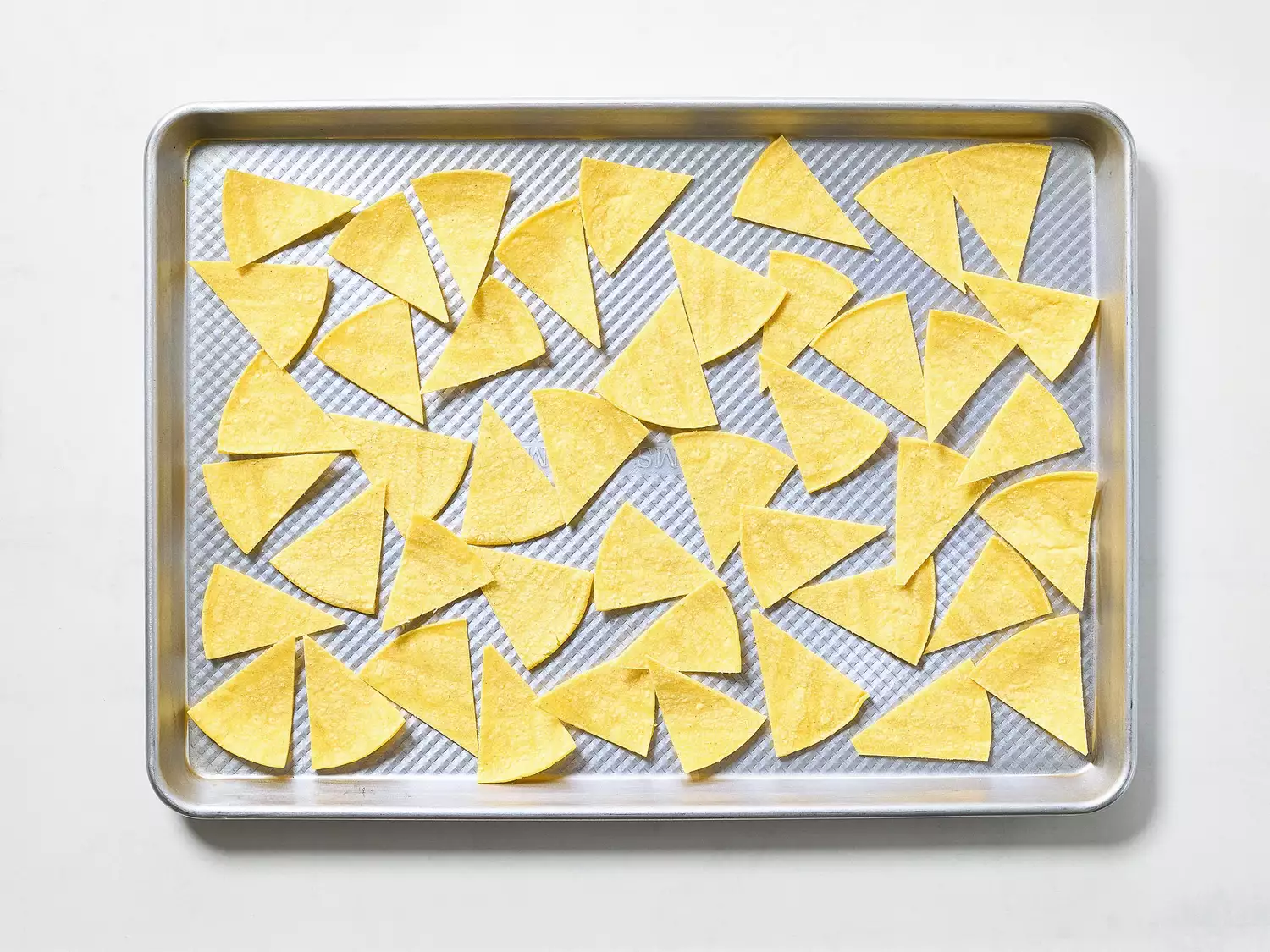 Tortilla wedges arranged on a baking sheet for chips.
