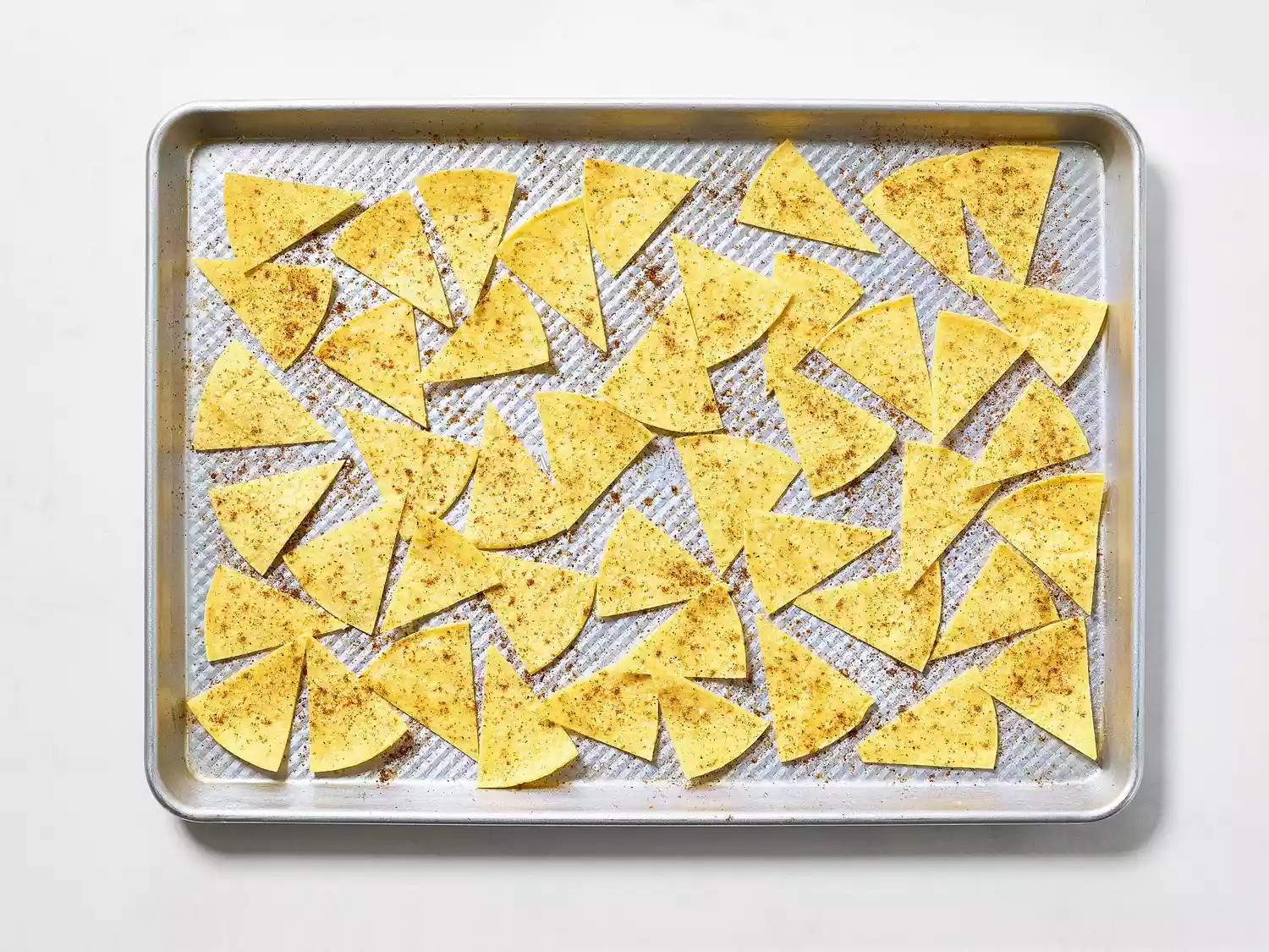 Seasoned tortilla wedges on a baking sheet before baking.