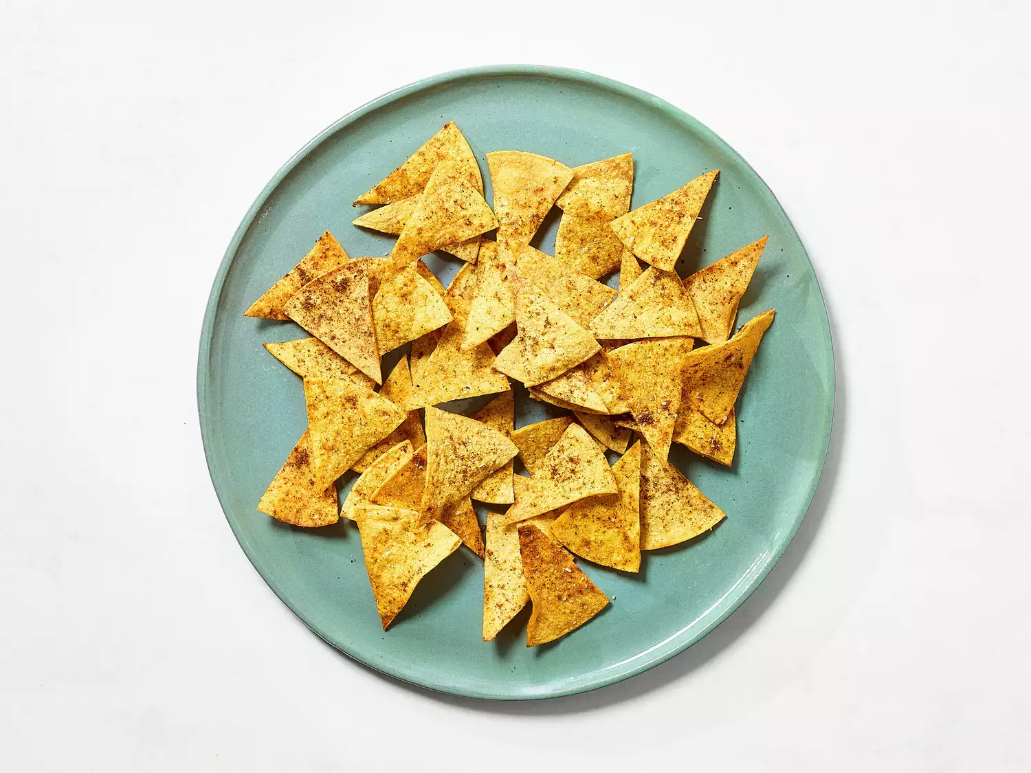 Homemade seasoned tortilla chips on a green plate.