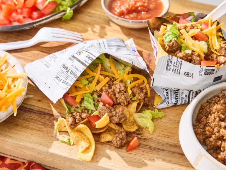 Opened taco in a bag filled with taco ingredients on wooden board next to different taco ingredients