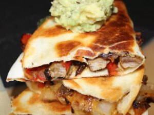Close up view of a sliced fajita quesadilla with guacamole on top on a plate