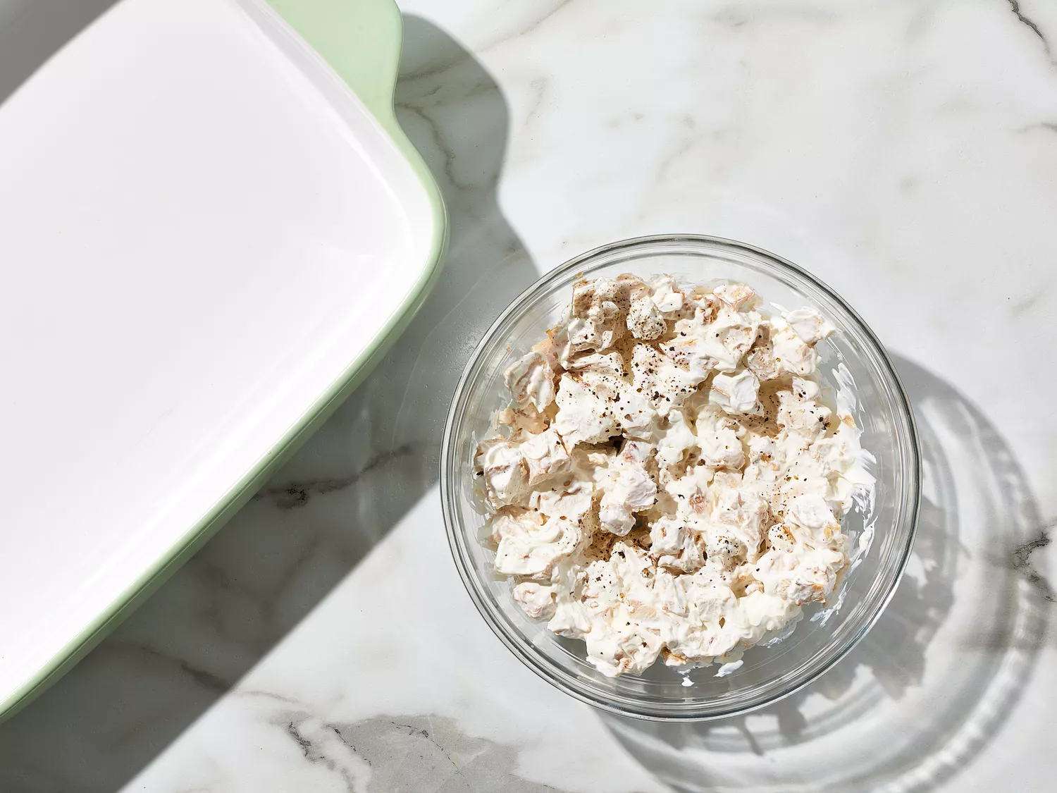 an overhead shot of a baking dish and chicken combined with sour cream, salt, and pepper in a glass bowl