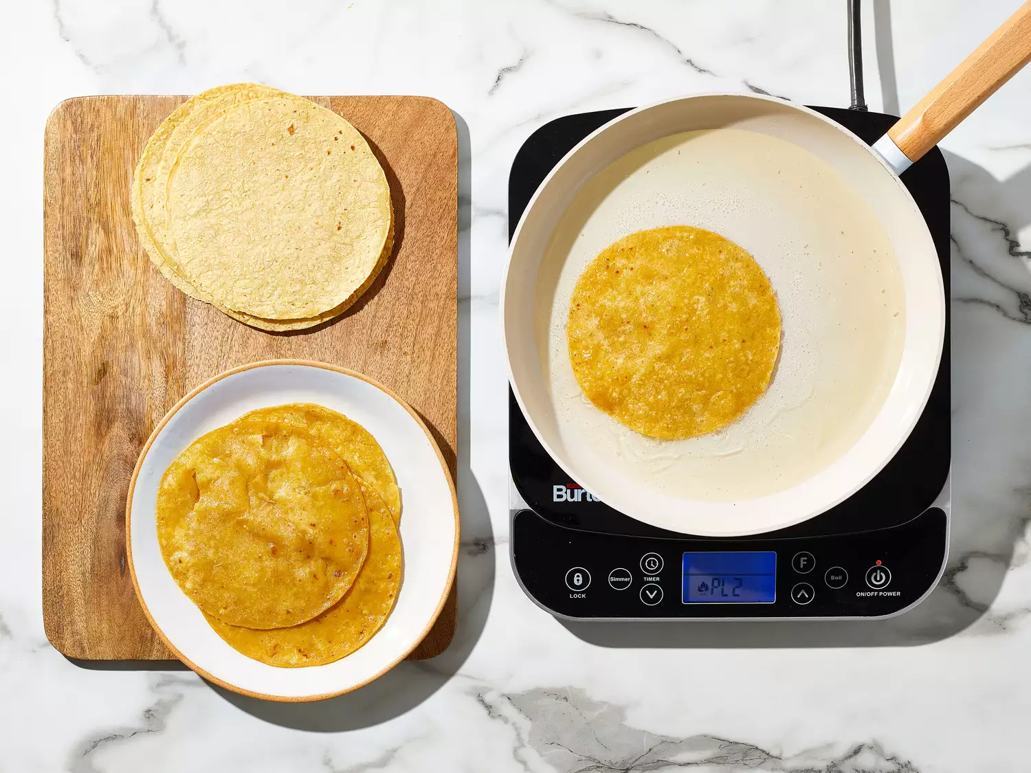 an overhead of tortillas cooking in a skillet and more tortillas on a cutting board