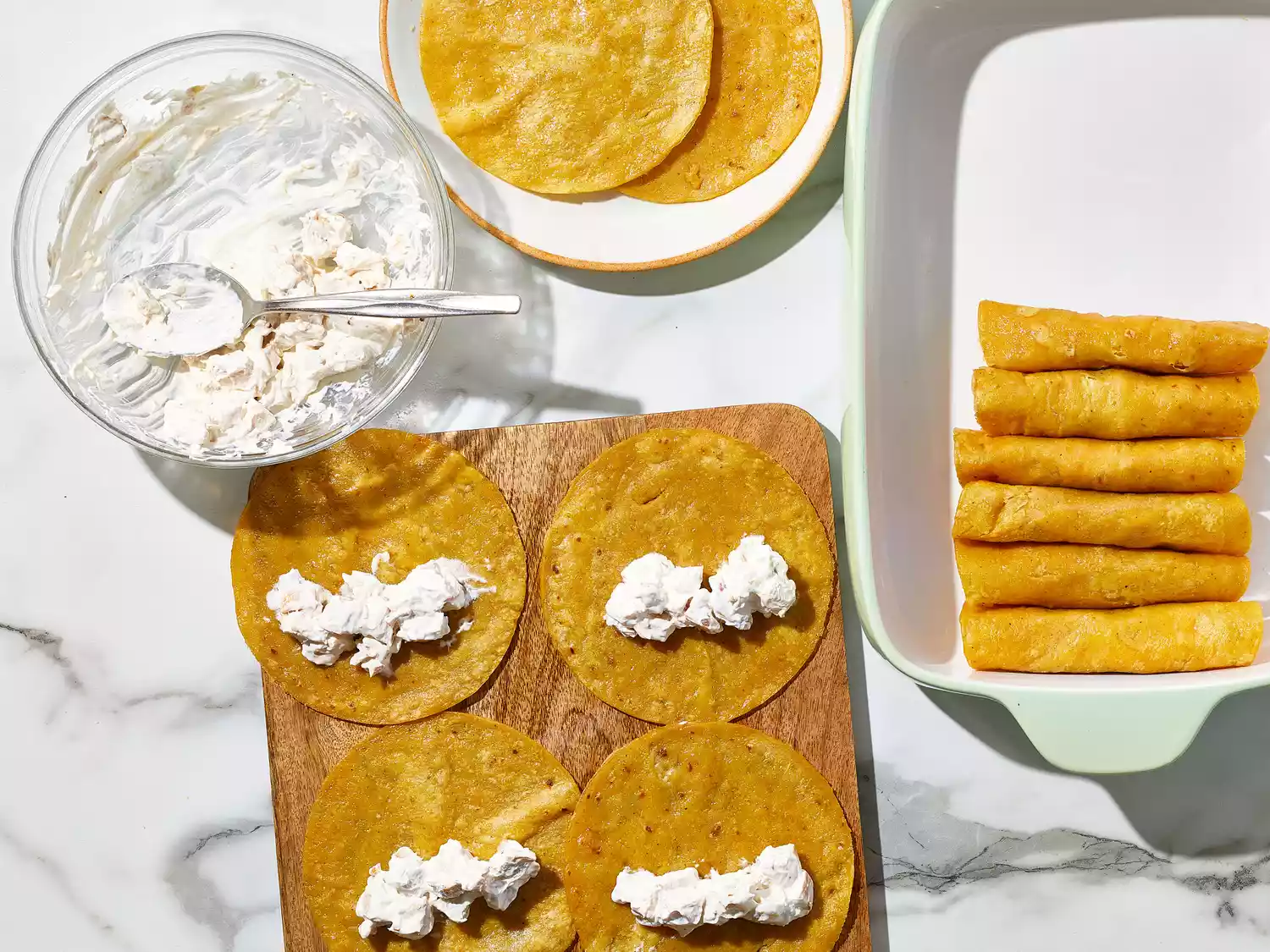 an overhead shot of enchiladas filled with sour cream chicken in a baking dish and more tortillas open on a cutting board topped with sour cream chicken
