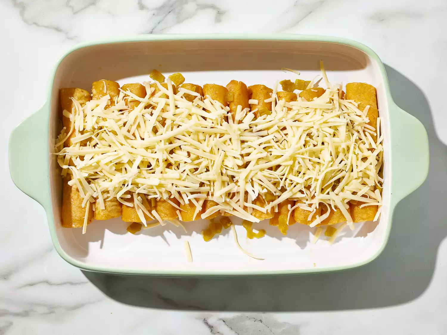 an overhead shot of chicken enchiladas topped with cheese in a baking dish