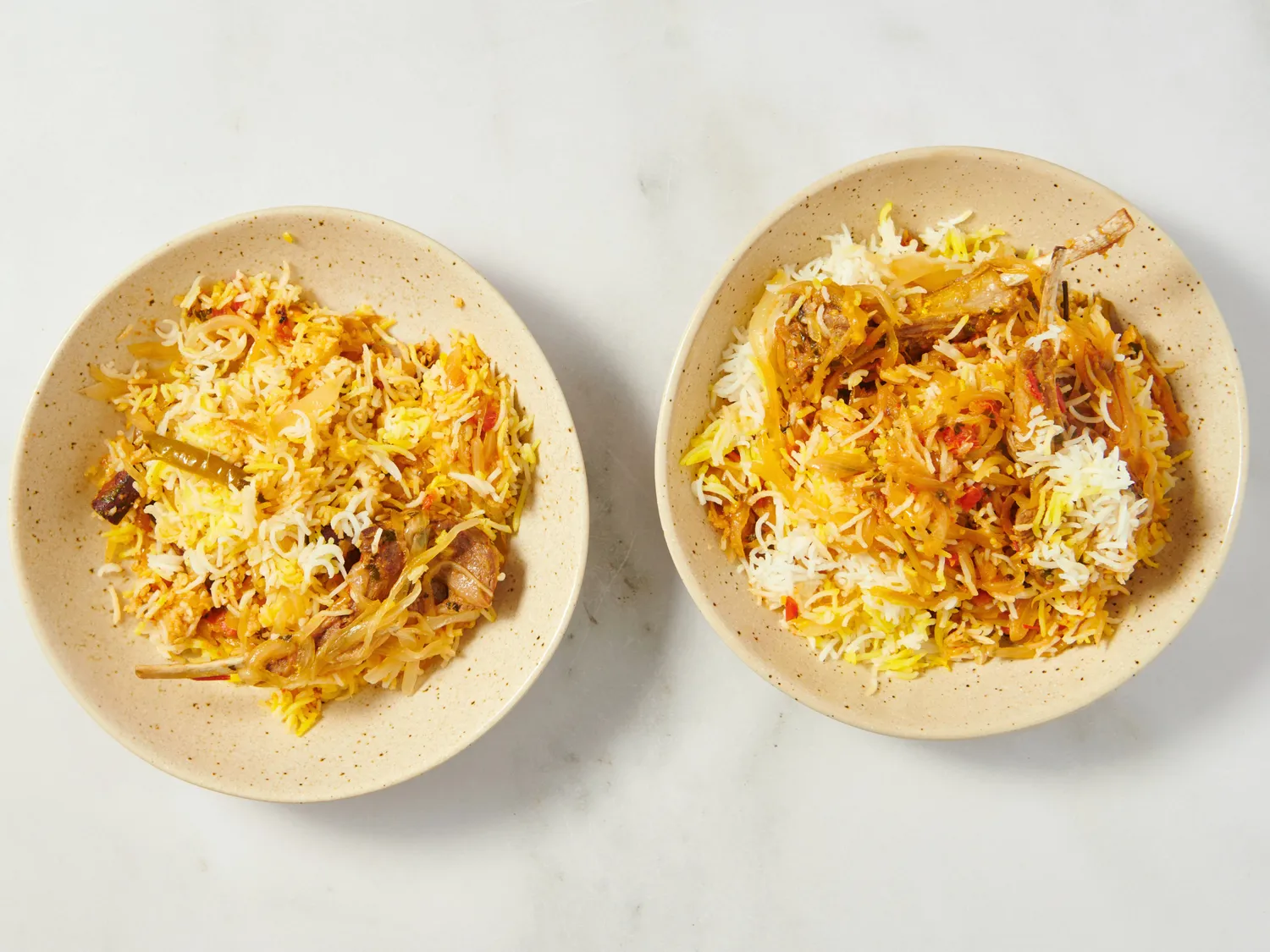 Two plates of lamb gosht biryani served on a white surface