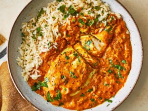 A close up, overhead view of a single bowl of indian chicken curry served with rice and fresh cilantro