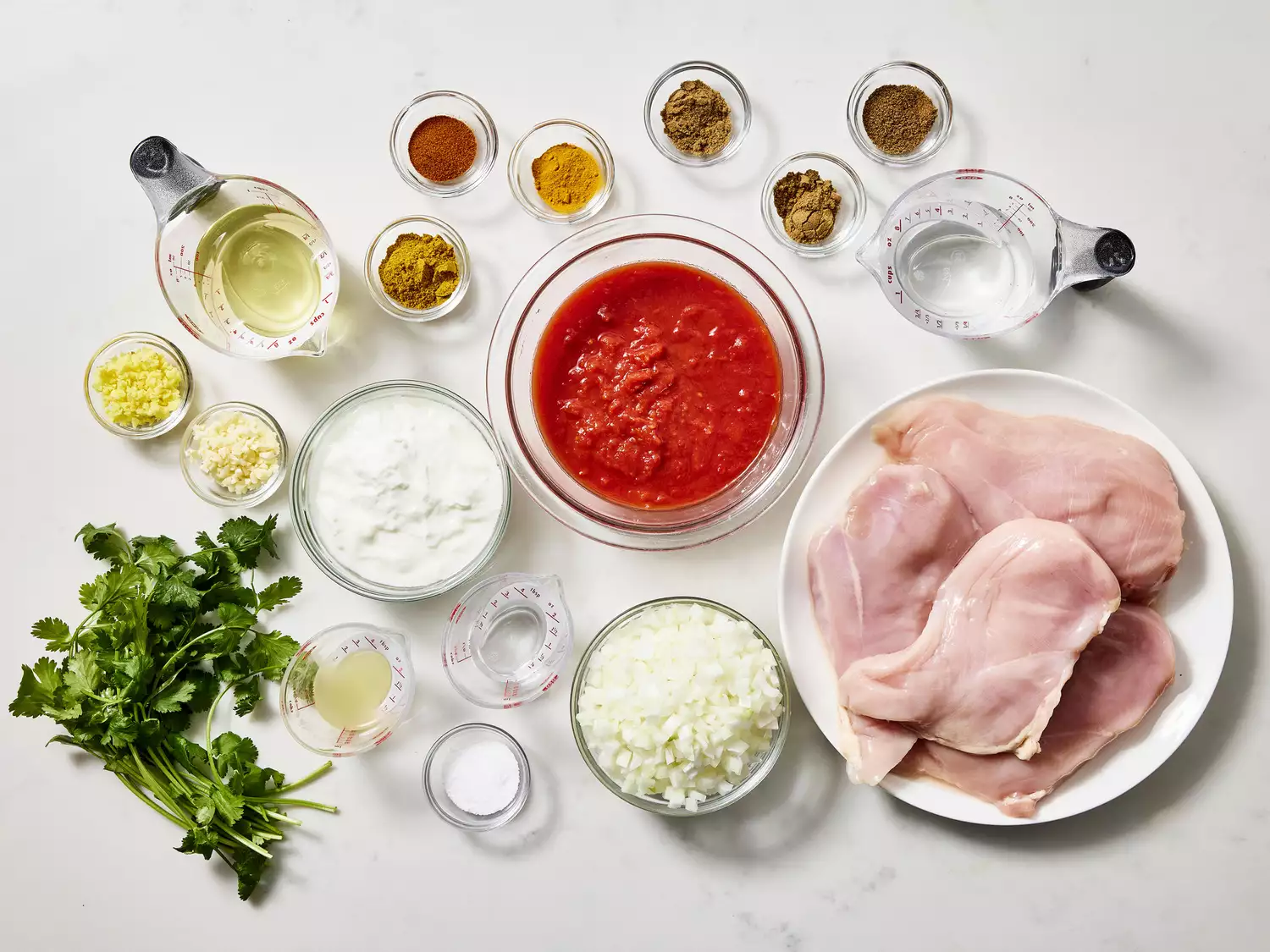 Ingredients for making Indian Chicken Curry (Murgh Kari) on a white surface.
